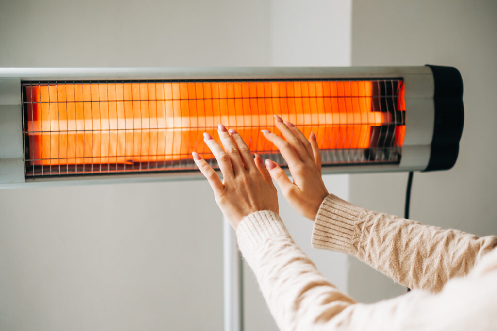 Woman warms up hands over a Halogen heater. Concept of the need for good central heating.